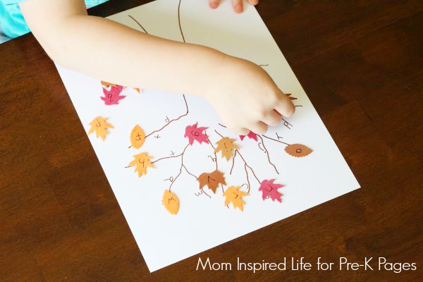 child placing leaves with letters onto a tree on paper
