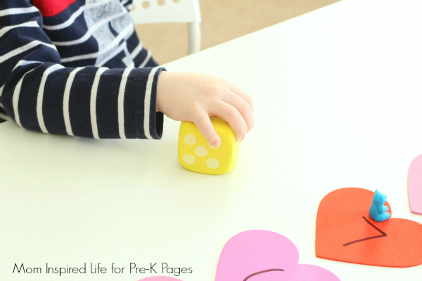 Valentine's Day Counting Game preschooler rolling a dice for the hearts number line counting game
