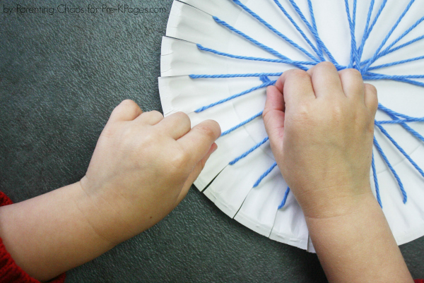child weaving yarn through paper plate