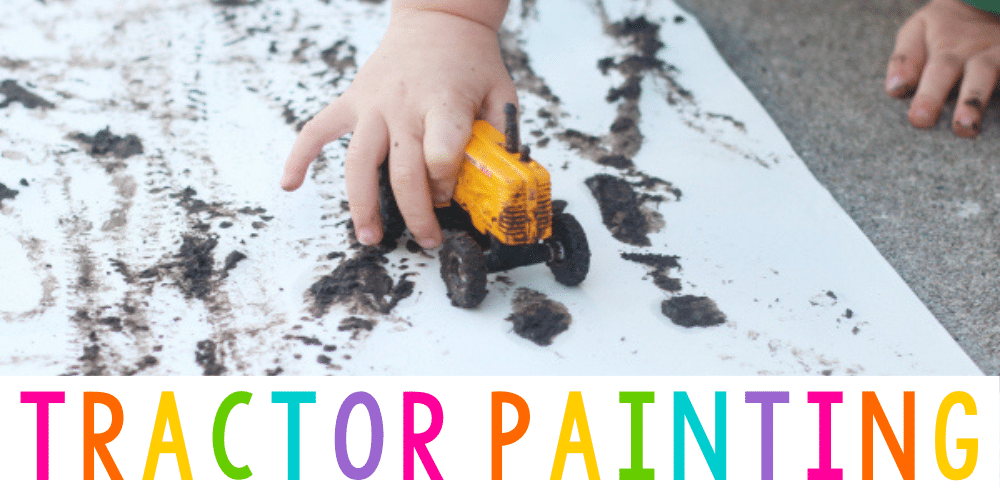 a childs hand holding a toy tractor on top of white paper covered in mud