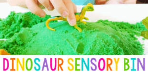 green sensory sand in tray with toy dinosaur